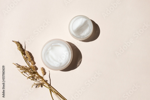 Moisturizer creams and dry meadow herbs on beige background, top view. Care for sensitive skin with natural extract. Summer or autumn skincare body care concept photo