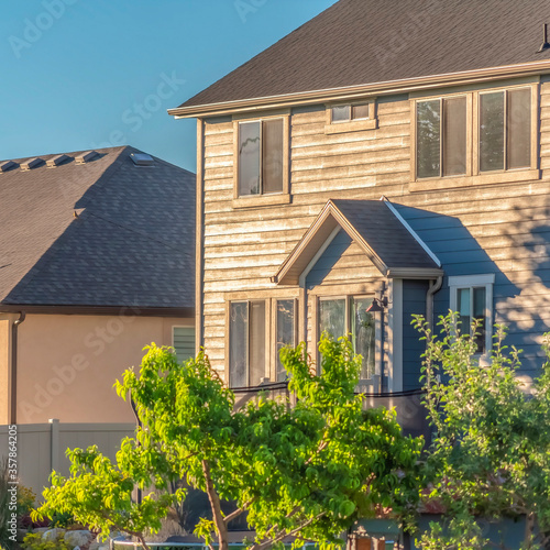 Square Sunny day view of home exterior with gray roof over sunlit wall and windows