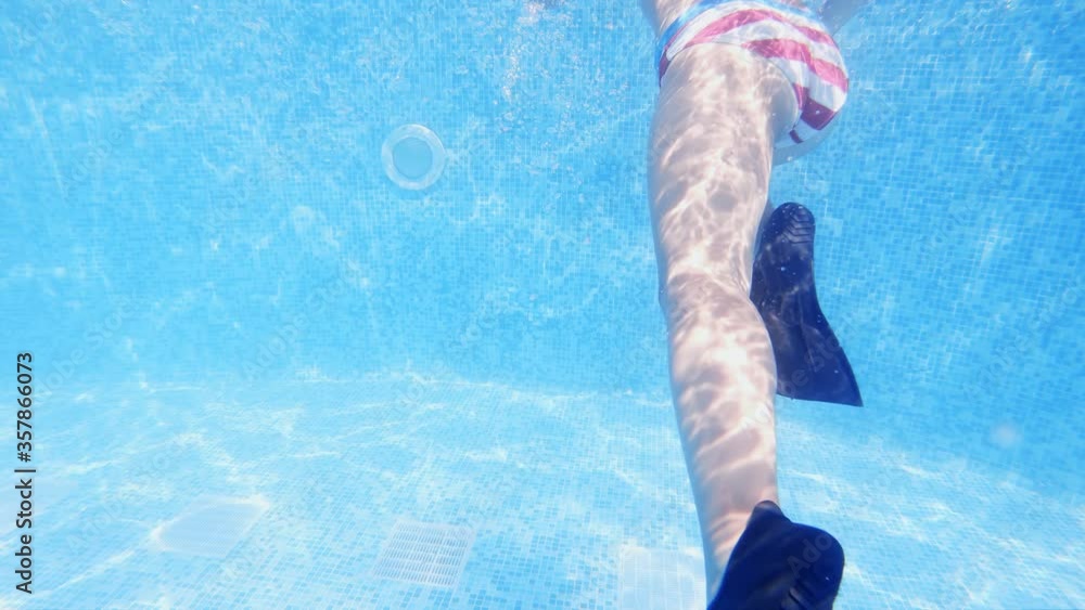 Cute girl with flippers in swimming pool at tropical beach, underwater view, slow motion