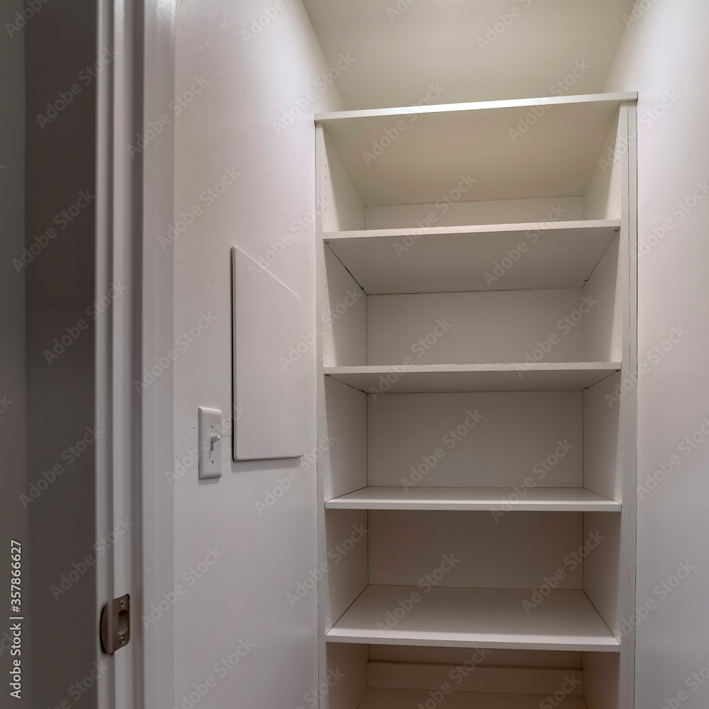 Square crop Walk in closet or pantry with empty wall shelves seen through open hinged door Square crop Walk in closet or pantry with empty wall shelves seen through open hinged door