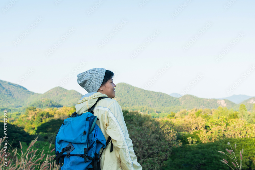 Asian young man in a yellow long shirt and gray hat hiking standing smiling and happy at green mountain peak above clouds Hiker outdoor. Lamphun Province, In the morning.