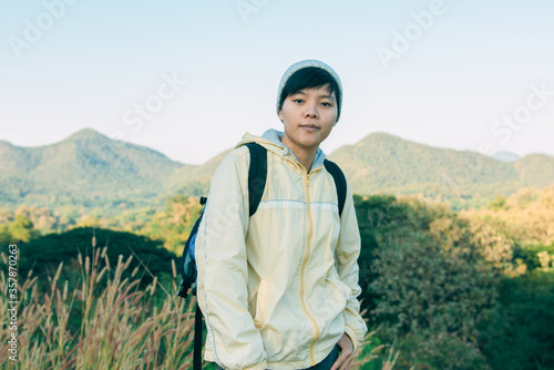 Asian young man in a yellow long shirt and gray hat hiking standing smiling and happy at green mountain peak above clouds Hiker outdoor. Lamphun Province, In the morning.