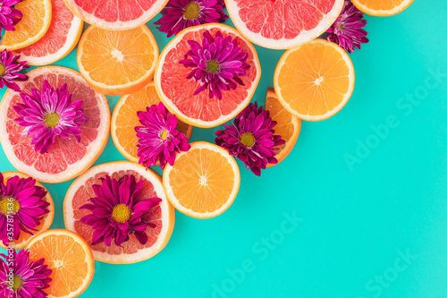 Colorful pattern composition made of slices of citrus fruits  orange  grapefruit  with purple flowers  in a turquoise background