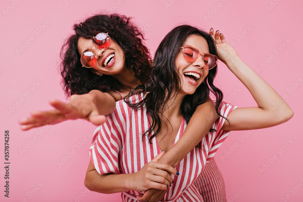 Obraz premium African girl hugs her sister and reaches for camera. Young women in high spirits posing over isolated background