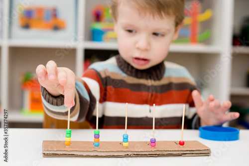 Home made montessori metodic tool for early education, learning to count. 2 year old boy puts beads on wooden rods. Children, people, infancy and education concept. Formation and development of the ch photo