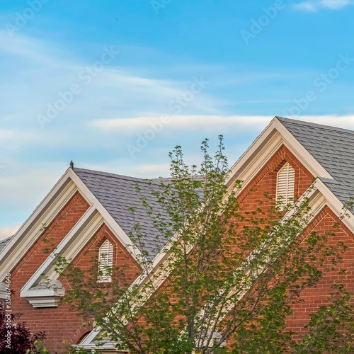 Square Weather vane and vent on top of the gray gable roof of home against blue sky