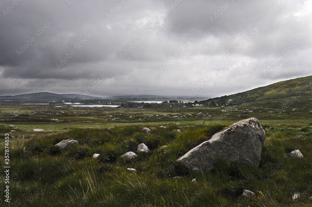 Vaste plaine verte, humide, rocheuse et herbeuse, parsemée de ruisseaux et de lacs sous un ciel nuageux et orageux dans le Connemara en Irlande.