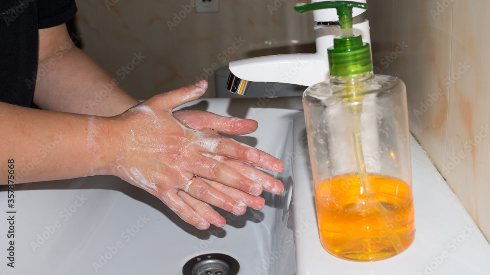 A man thoroughly washes his hands with soap in the bathroom, in a white washbasin with a white tap and antibacterial soap, makes a lot of foam and washes fingers and brushes after walking on the stree