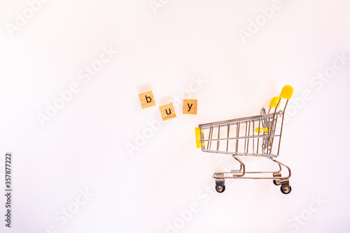 Wooden letters for the word "buy" with yellow shopping cart white background.