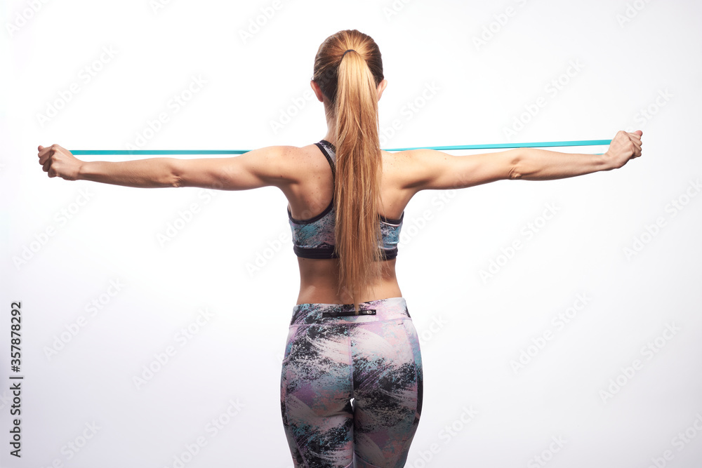 Blonde fitness girl giving her backwith a ponytail wearing sport clothes stretching an elastic training band with her hands Blonde fitness girl giving her backwith a ponytail wearing sport clothes stretching an elastic training band with her hands