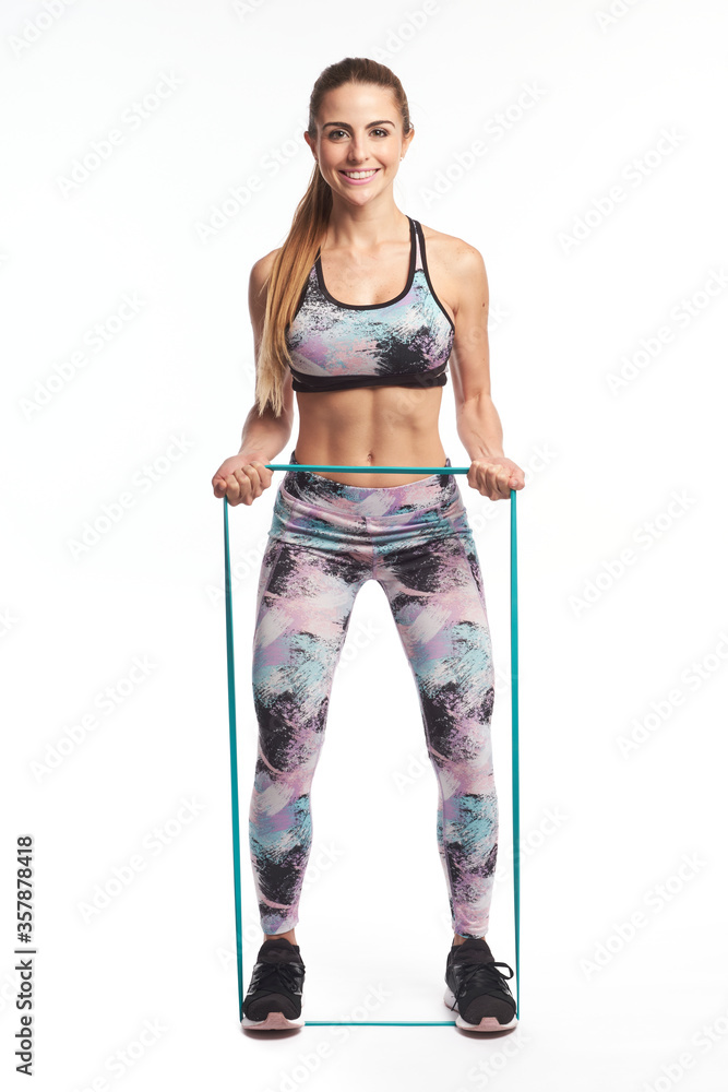 Blonde fitness girl wearing sport clothes strechting an elastic training band with her hands while standing up looking at camera Blonde fitness girl wearing sport clothes strechting an elastic training band with her hands while standing up looking at camera
