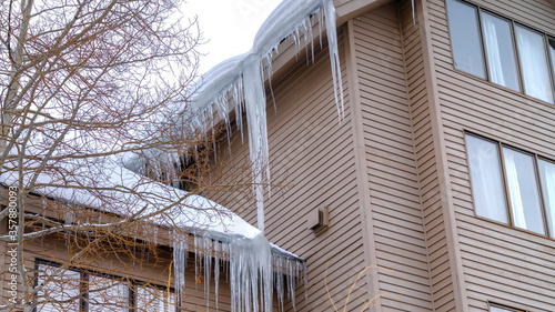 Panorama Home exterior with sharp icicles at the edge of roofs with thick layer of snow