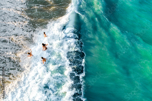 Drone view of group of children playing in the sea waves, kids getting hit by wave 