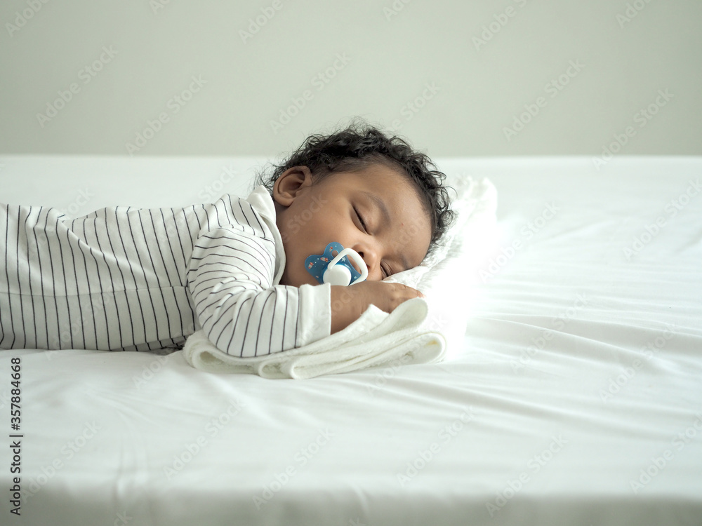 African baby boy is sleeping. Baby sucks pacifier. Stock Photo | Adobe Stock