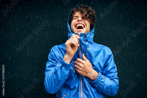 Foto Happy man smiling broadly, wearing blue raincoat during the rain outside