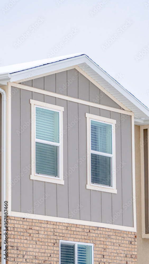 Vertical crop Snowy roof brick wall and vertical siding at exterior of townhome against sky Vertical crop Snowy roof brick wall and vertical siding at exterior of townhome against sky