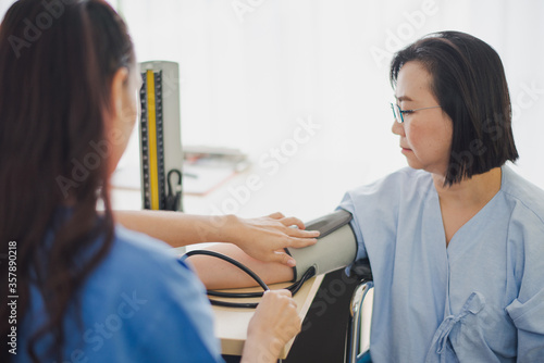 Young Asian woman doctor measure blood pressure of elderly patient sitting in Wheelchair at hospital which excite felling serious. Medicine and health care safe concept