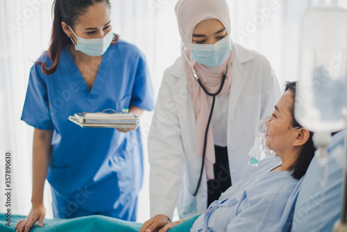 Photography Young Asian woman Muslim doctor and nurse giving advice discussion and check up to elderly patient sitting in bed at hospital which smiling and felling happy