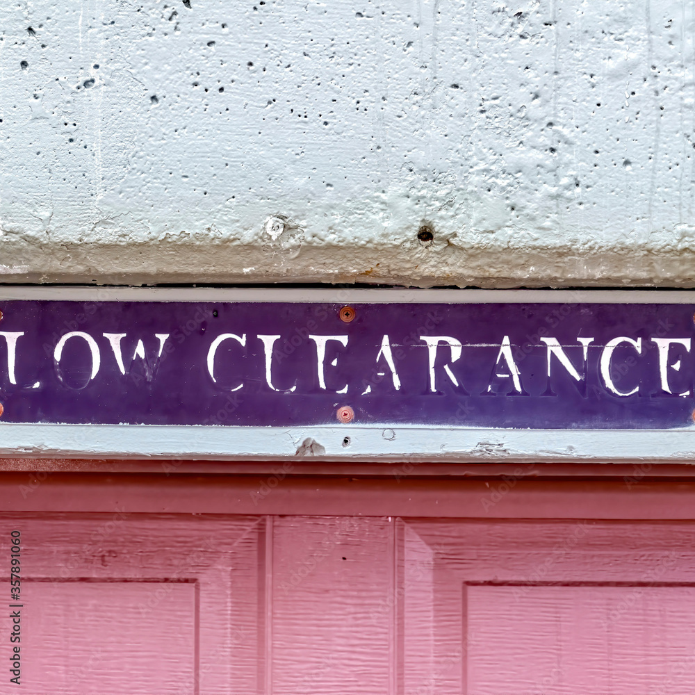 Square crop Low Clearance sign above the panelled red wooden garage door of a building