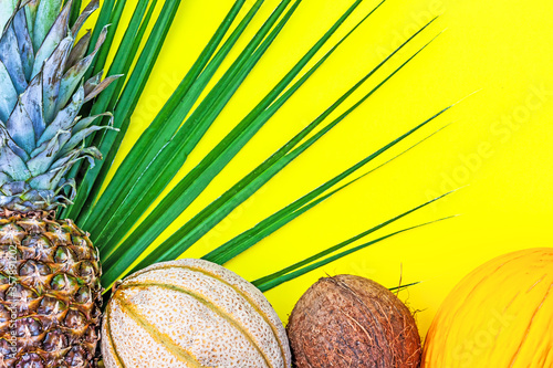 Summer creative tropic fuit layout. Pineapple, melon, lemon, orange, coconut and palm leaf on yellow background. Healthy food summertime concept. Top view. Copy space