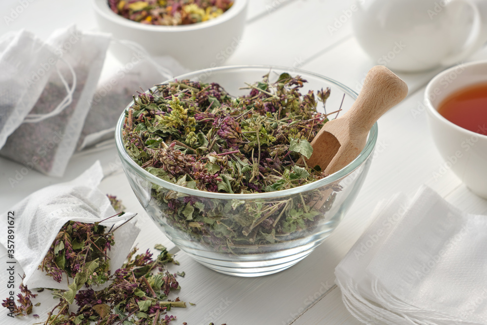 Bowl of dry Origanum vulgare flowers, tea bags filled with wild marjoram flowers. Tea cup and teapot on wooden table. Alternative medicine. Bowl of dry Origanum vulgare flowers, tea bags filled with wild marjoram flowers. Tea cup and teapot on wooden table. Alternative medicine.