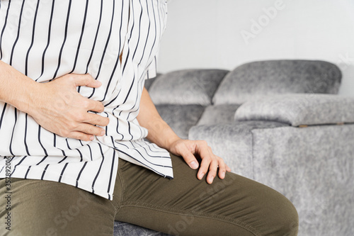 Young man suffering from abdominal pain while sitting on sofa at home. Healthcare medical or daily life concept.
