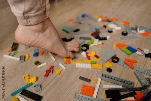 Foot stepping on plastic construction toys. Scattered toys on the floor. Gets severe pain.