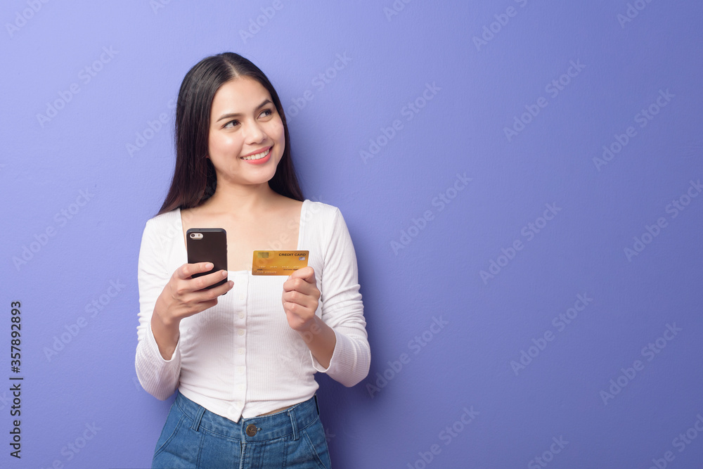 Portrait of Young Asian woman is using cell phone with credit card on purple background Portrait of Young Asian woman is using cell phone with credit card on purple background