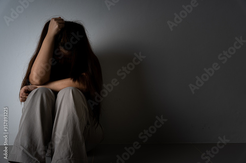 sad woman hug her knee and cry sitting alone in a dark room. Depression, unhappy, stressed and anxiety disorder concept.