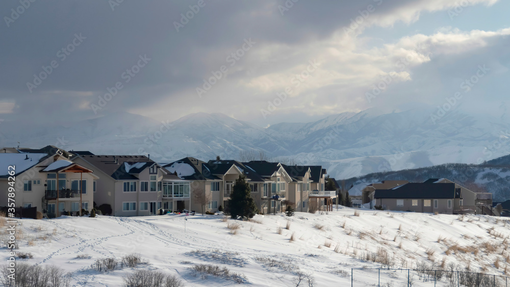 Panorama crop Homes on snowy terrain ovelooking Wasatch Mountain peak and dark overcast sky Panorama crop Homes on snowy terrain ovelooking Wasatch Mountain peak and dark overcast sky