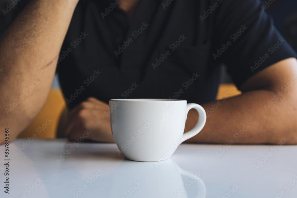 closeup hand of a businessman holding a white cup of coffee in the room with soft-focus and over light in the background