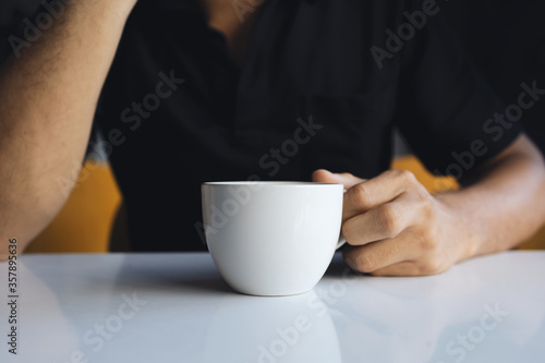 closeup hand of a businessman holding a white cup of coffee in the room with soft-focus and over light in the background