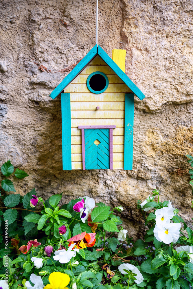 Cabane (nichoir) à oiseaux en bois colorée jaune et bleu. accrochée sur une mur. Fleurs de pensées.