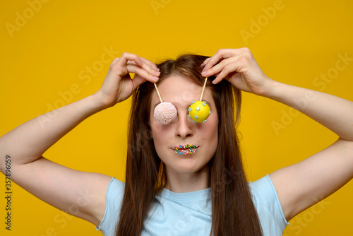 young european woman playes with cake pops on yellow background