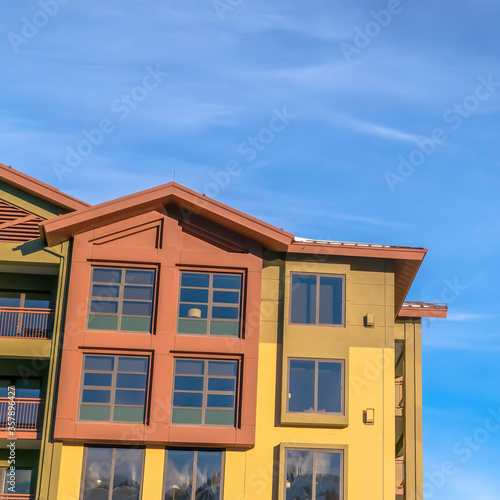Square Home exterior with balconies and multi color walls against blue sky and clouds