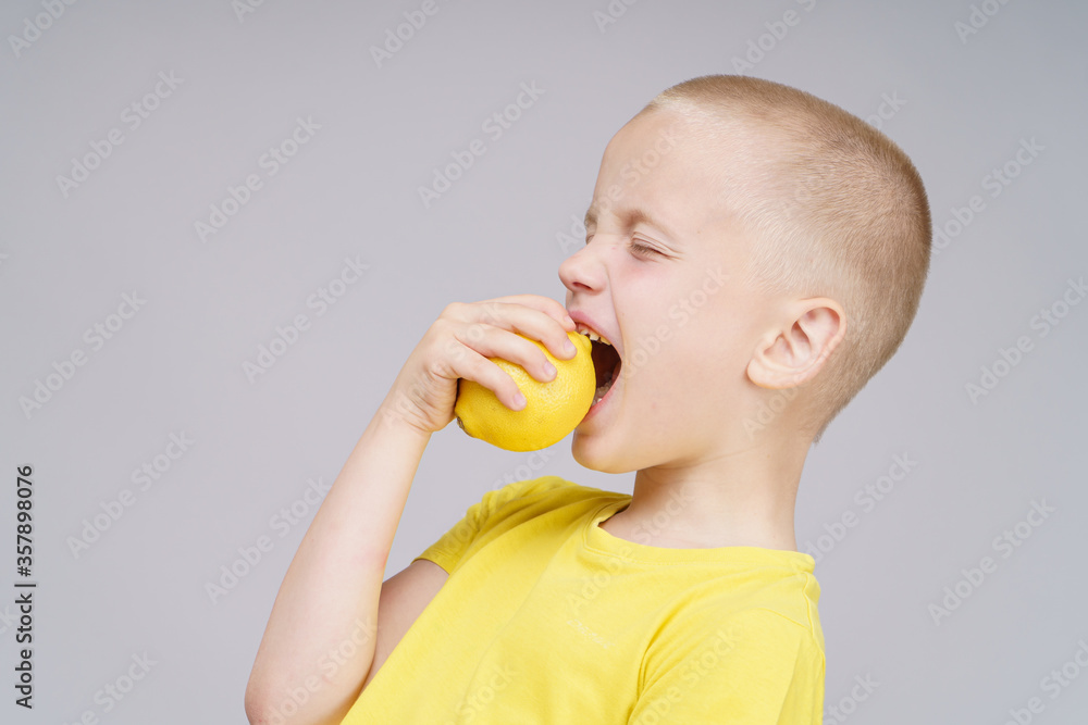 Smiling boy standing with fruit lemon. Isolated on gray Smiling boy standing with fruit lemon. Isolated on gray