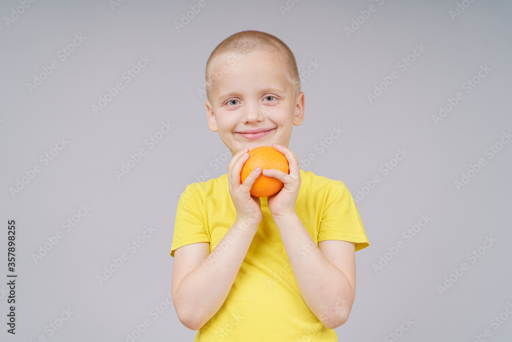 Smiling boy standing with fruit orange. Isolated on gray Smiling boy standing with fruit orange. Isolated on gray