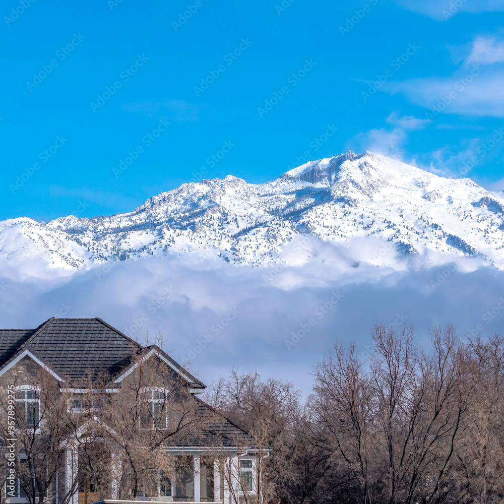 Square frame Sunlit snowy mountain with peak over low gray clouds against vibrant blue sky