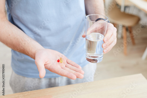 Close-up of male hand holding vitamin pill and glass of water he drinking vitamins in the morning