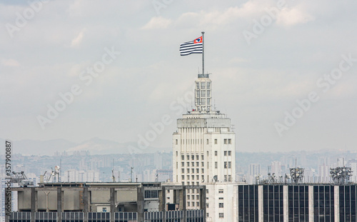 Topo do edifício Altino Arantes, com a bandeira do Estado de São Paulo ao vento e a cidade no horizonte.