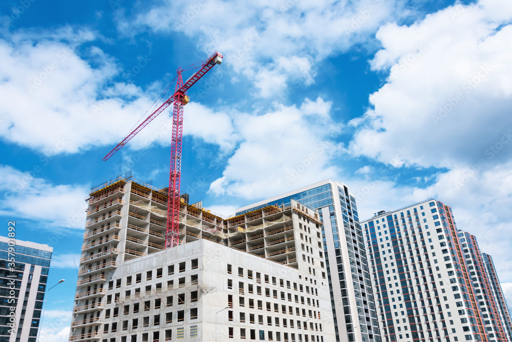 View of a multistorey building under construction with high construction cranes and a glass tower in the background clouds blue sky. View of a multistorey building under construction with high construction cranes and a glass tower in the background clouds blue sky.