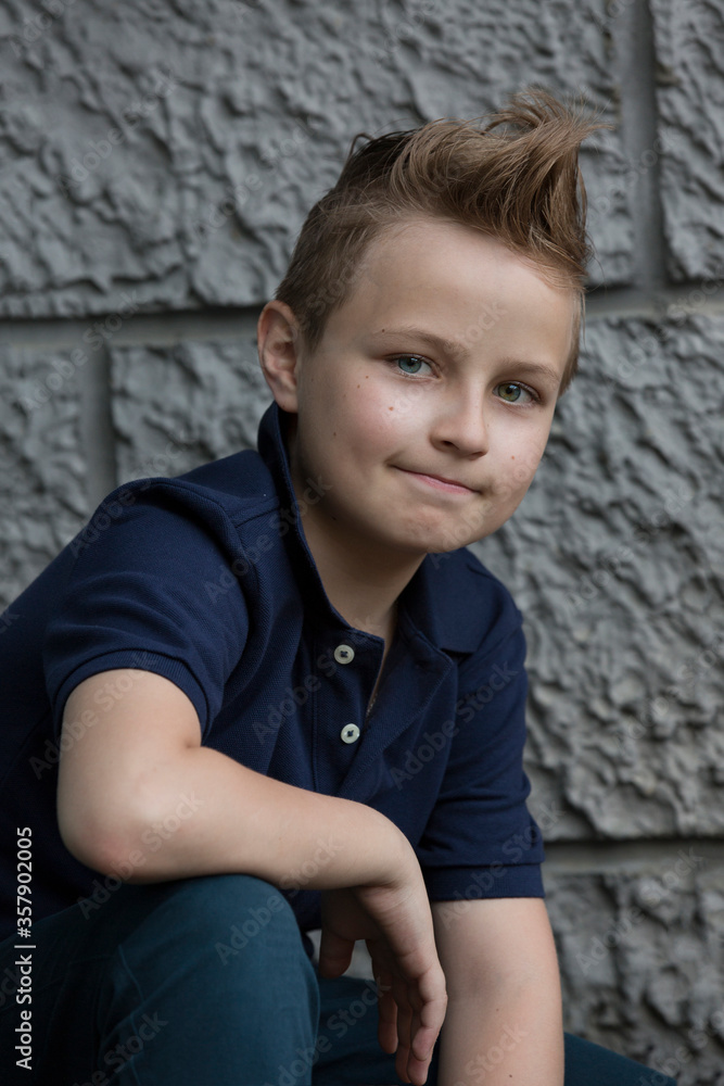 A handsome boy with a fashion haircut is standing by the wall in the street. He is 13 years old. The eyes of the boy are different colors, blue and green. A handsome boy with a fashion haircut is standing by the wall in the street. He is 13 years old. The eyes of the boy are different colors, blue and green.