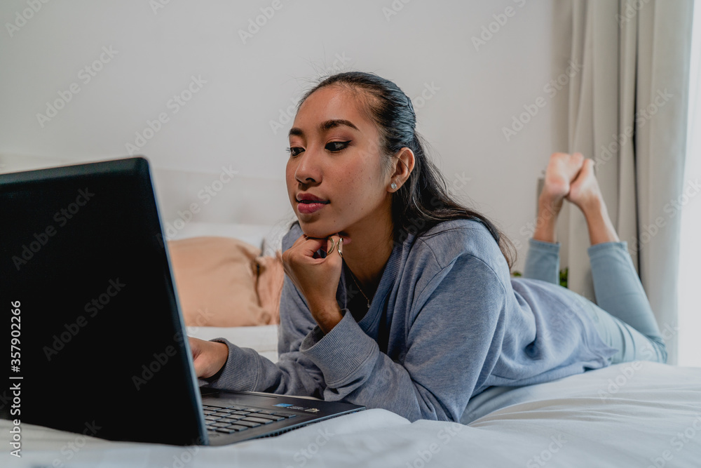 The girl with a light blue sweatshirt works at home. Lying on the bed with a laptop. Interior, house. The girl with a light blue sweatshirt works at home. Lying on the bed with a laptop. Interior, house.