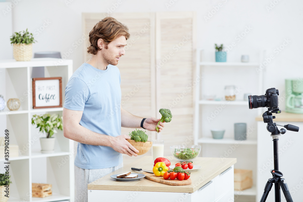 Young man holding vegetables in his hand and talking about the healthy food on the camera for his blog Young man holding vegetables in his hand and talking about the healthy food on the camera for his blog