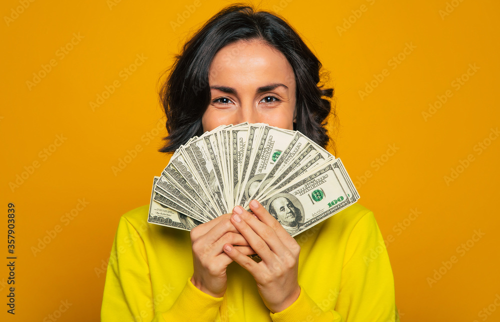 Here is my salary! Close-up photo of a young girl in a yellow hoodie, smiling with her eyes, hiding her face behind big amount of money in her hands. Here is my salary! Close-up photo of a young girl in a yellow hoodie, smiling with her eyes, hiding her face behind big amount of money in her hands.