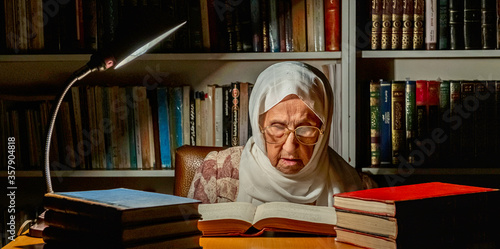 Arabic muslim old woman reading books at night with table lamp light photo