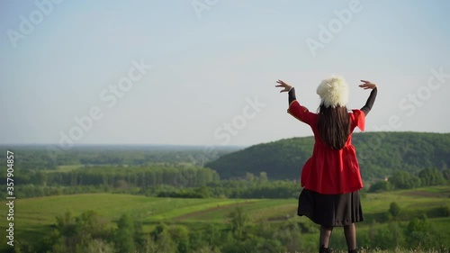 Georgian girl in white papakha and red national dress dances national dance named: rachuli, acharuli, osuri, shalaxo, mtiuluri. on the green hills of Georgia background. Georgian culture lifestyle. photo