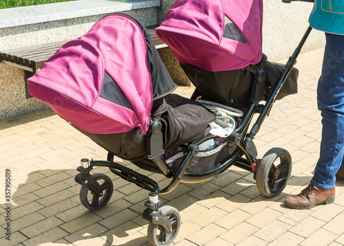 active mom walking in the park with a double twin stroller with two children