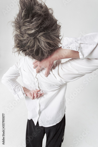 Androgyne in white shirt worn reverse side moving strangely with her hands at the back. Isolated vertical photo on white background.