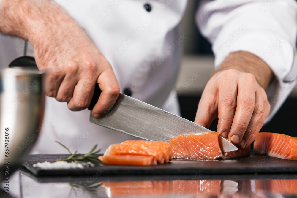Chef cutting fish fillet. Closeup chef hands cut salmon at kitchen table.